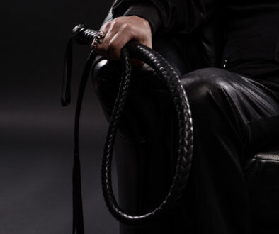 Male hand holding black leather whip